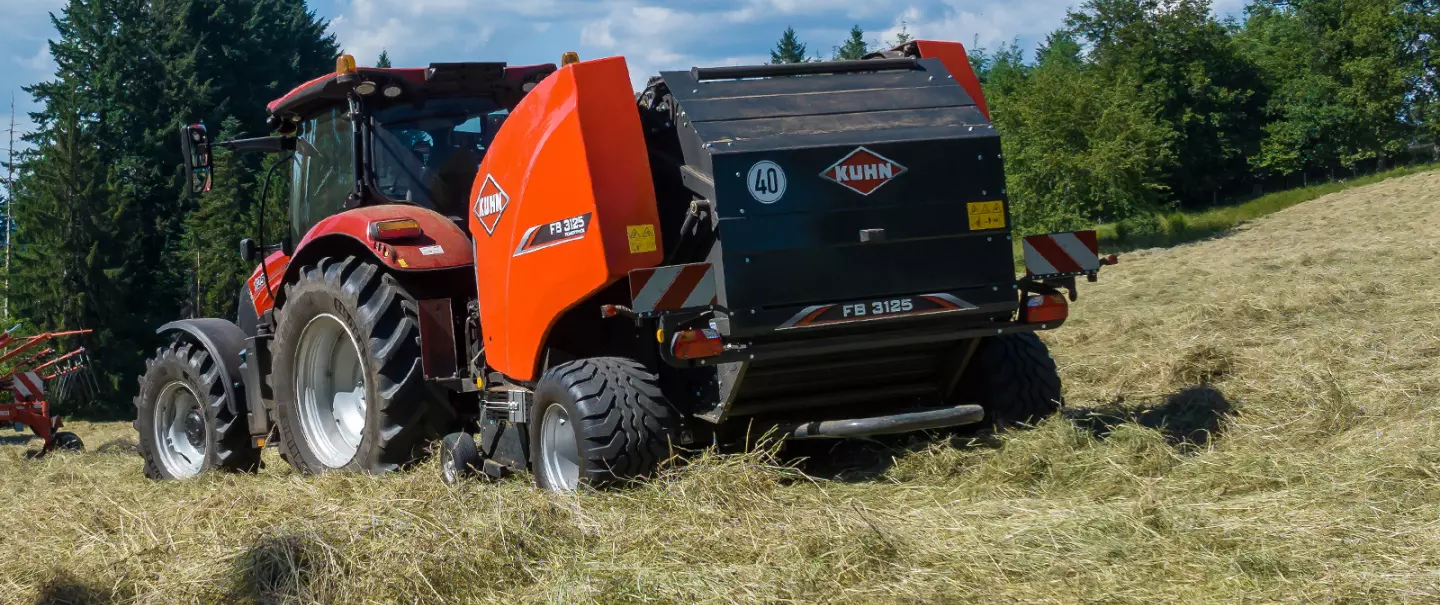 Рулонний прес-підбирач KUHN FB 3125 з фіксованою камерою та оператор у полі на задньому плані